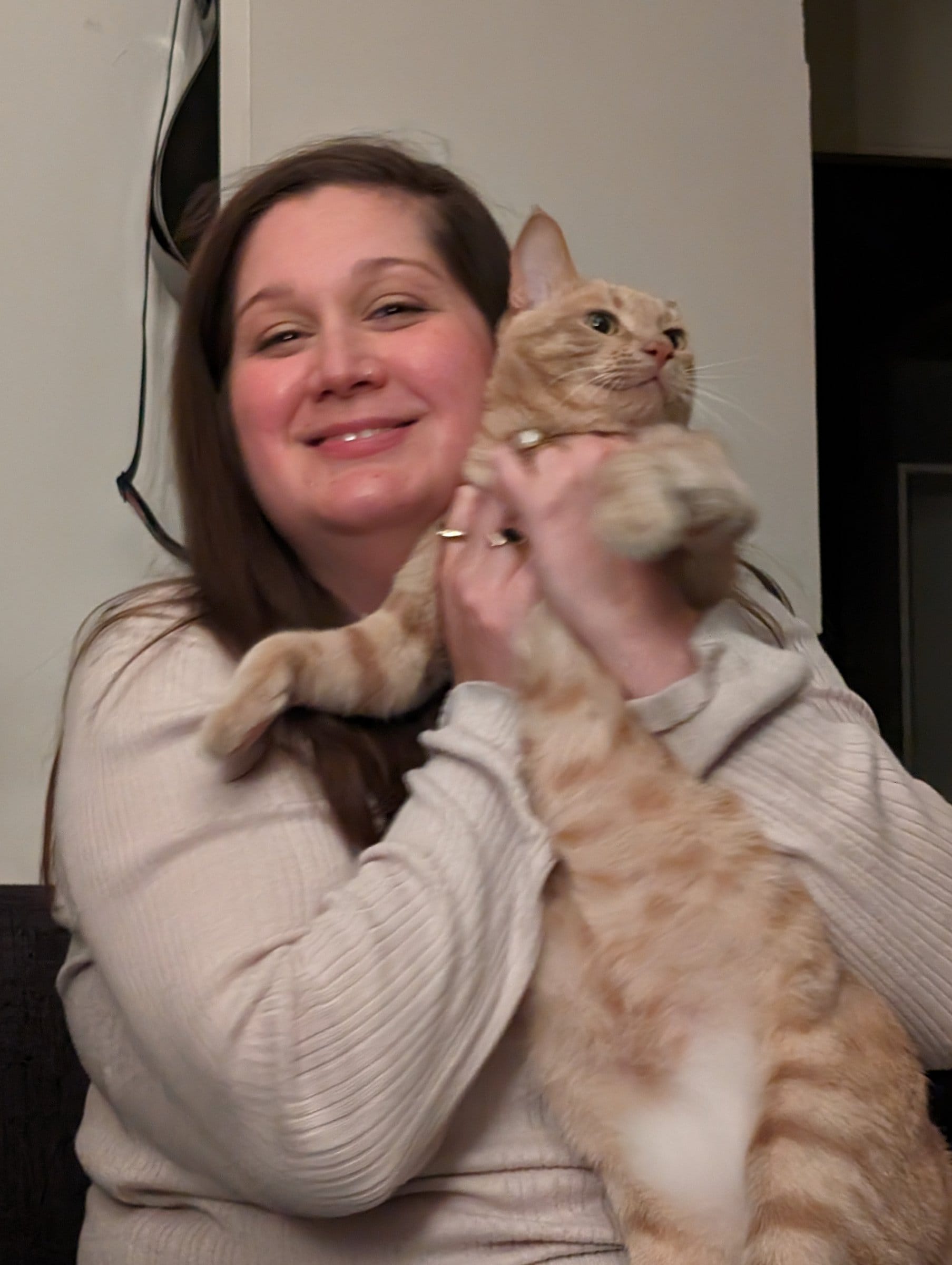 A smiling woman hugs a cream and ginger tabby.